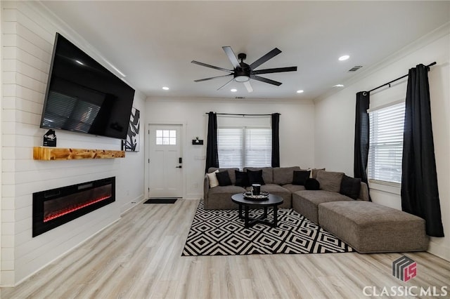 living room with ceiling fan, crown molding, a fireplace, and light hardwood / wood-style flooring