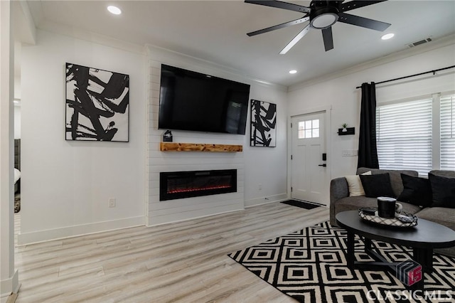 living room with ceiling fan, a large fireplace, ornamental molding, and light hardwood / wood-style flooring