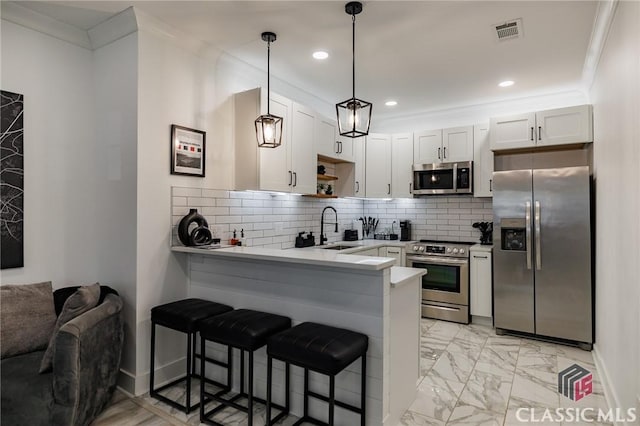 kitchen with white cabinets, appliances with stainless steel finishes, decorative light fixtures, a kitchen bar, and kitchen peninsula