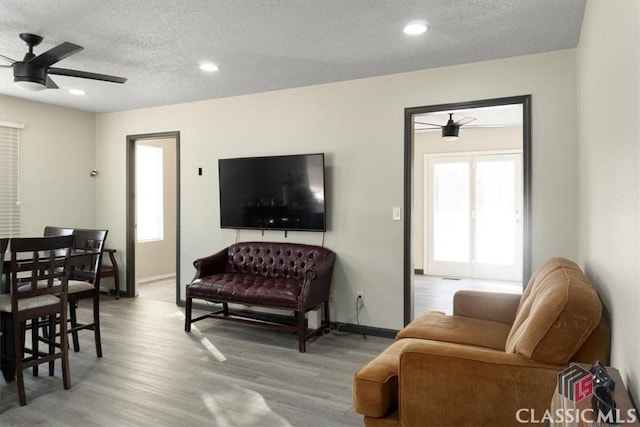 living room with ceiling fan, light hardwood / wood-style floors, and a textured ceiling