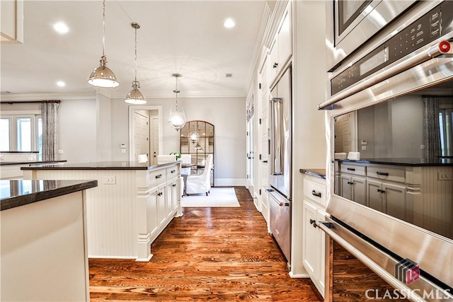 kitchen with dark hardwood / wood-style floors, pendant lighting, double oven, white cabinetry, and a kitchen island with sink