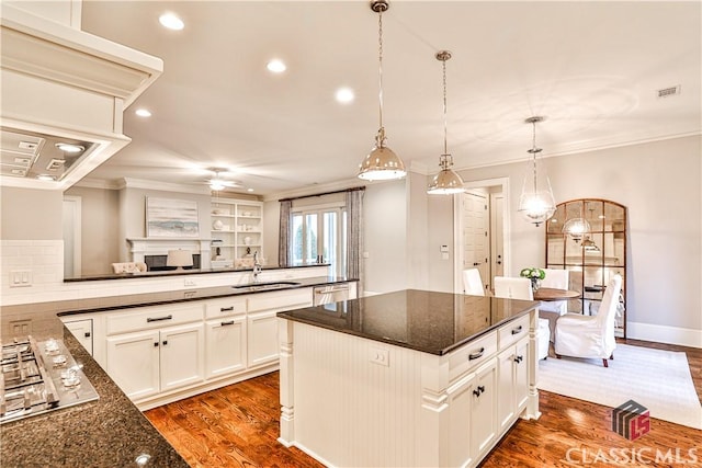 kitchen featuring appliances with stainless steel finishes, pendant lighting, dark hardwood / wood-style flooring, dark stone counters, and a center island