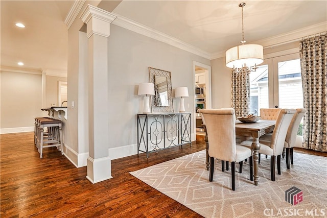 dining space featuring dark wood-type flooring, an inviting chandelier, crown molding, and decorative columns