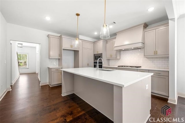 kitchen featuring premium range hood, stainless steel microwave, black gas cooktop, and an island with sink