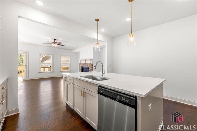 kitchen featuring dishwasher, sink, hanging light fixtures, a kitchen island with sink, and a brick fireplace