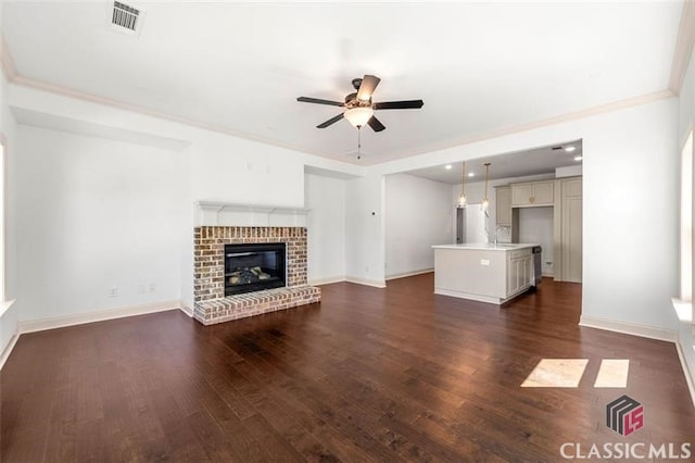 unfurnished living room featuring a fireplace, sink, ornamental molding, ceiling fan, and dark hardwood / wood-style floors