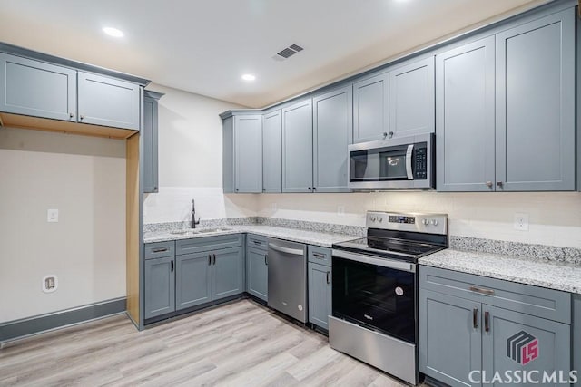 kitchen with stainless steel appliances, tasteful backsplash, gray cabinetry, and light stone counters