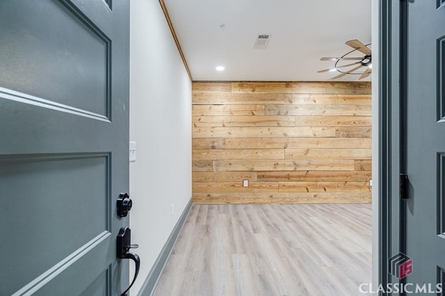 unfurnished living room with light hardwood / wood-style flooring, sink, wooden walls, and ceiling fan