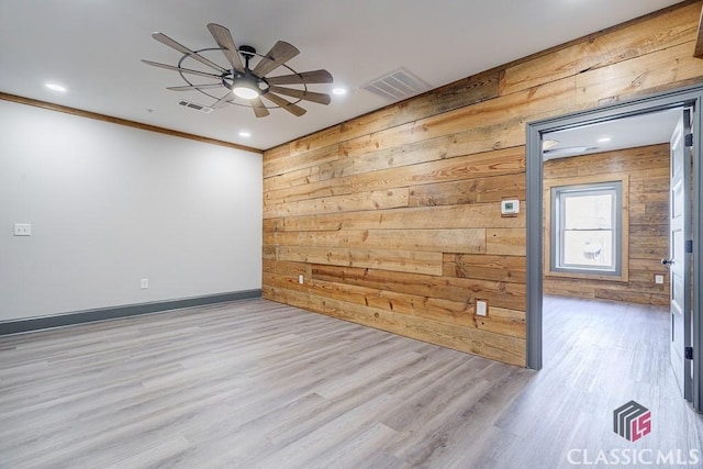 empty room featuring ceiling fan, ornamental molding, light wood-type flooring, and wood walls