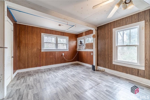 spare room featuring beamed ceiling, a wealth of natural light, light hardwood / wood-style floors, and wood walls