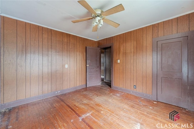 unfurnished bedroom featuring hardwood / wood-style flooring, crown molding, ceiling fan, and wood walls