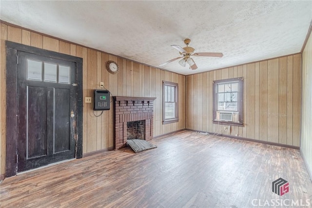 unfurnished living room featuring ceiling fan, cooling unit, a fireplace, a textured ceiling, and light wood-type flooring