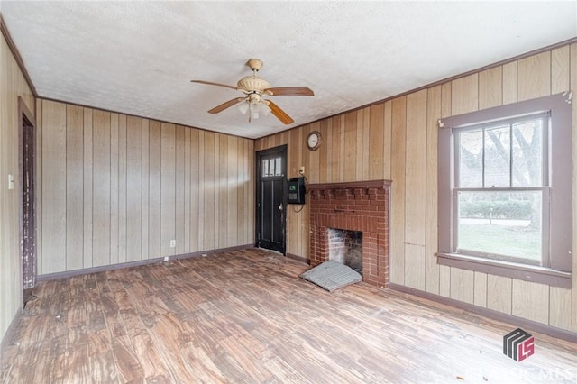 unfurnished living room featuring wood walls, a textured ceiling, a brick fireplace, hardwood / wood-style flooring, and ceiling fan