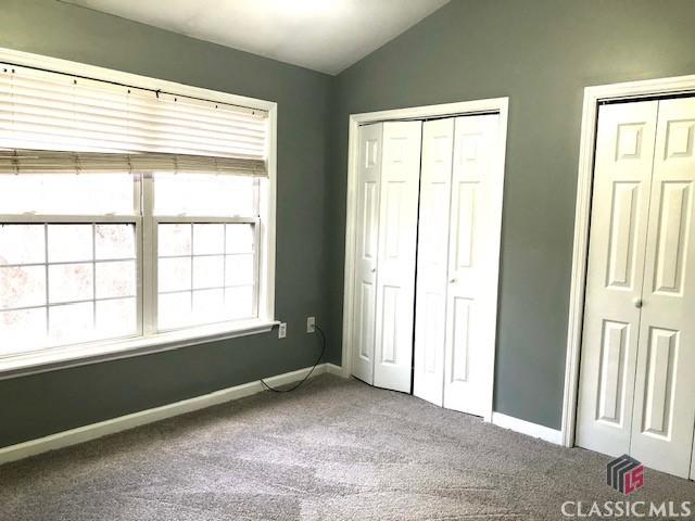 unfurnished bedroom with lofted ceiling, two closets, and carpet floors