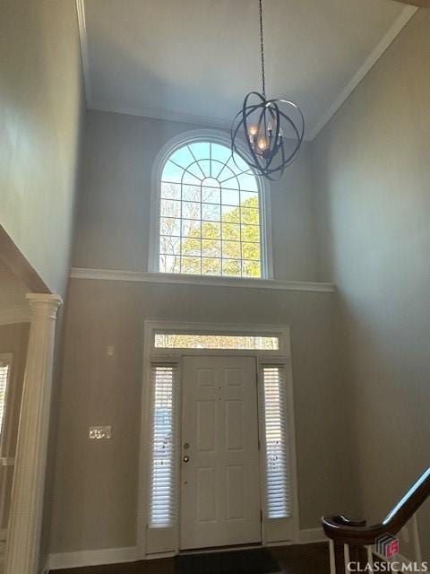 foyer entrance featuring an inviting chandelier, ornamental molding, a high ceiling, and ornate columns