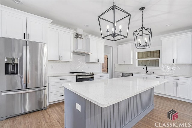 kitchen featuring a kitchen island, appliances with stainless steel finishes, decorative light fixtures, white cabinetry, and wall chimney range hood