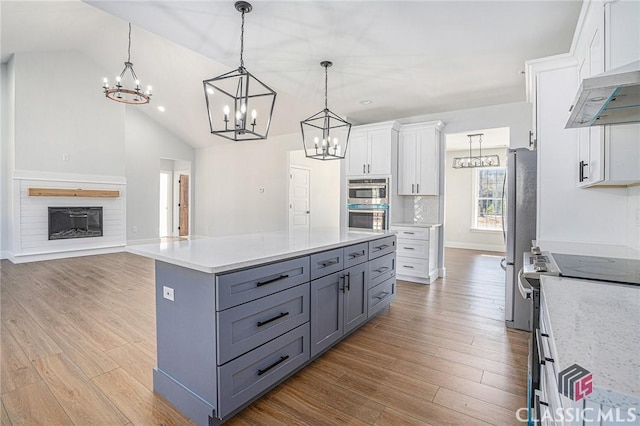 kitchen featuring vaulted ceiling, appliances with stainless steel finishes, decorative light fixtures, white cabinetry, and light hardwood / wood-style floors