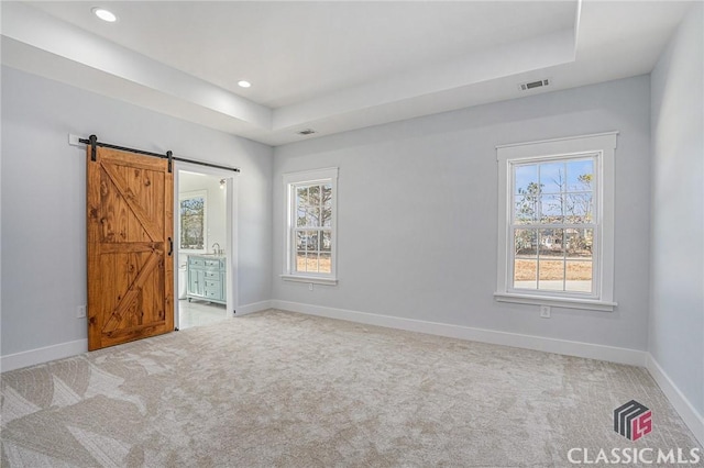 unfurnished bedroom with multiple windows, a barn door, carpet, and ensuite bath