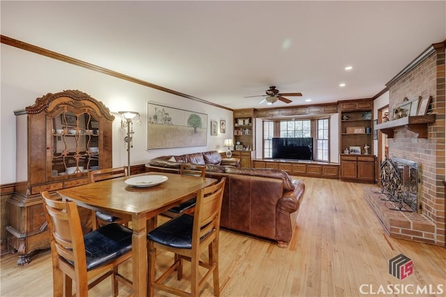 dining space featuring light hardwood / wood-style flooring, ceiling fan, a fireplace, ornamental molding, and built in shelves