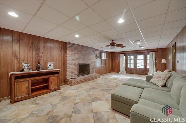 living room with a fireplace, wooden walls, french doors, and ceiling fan