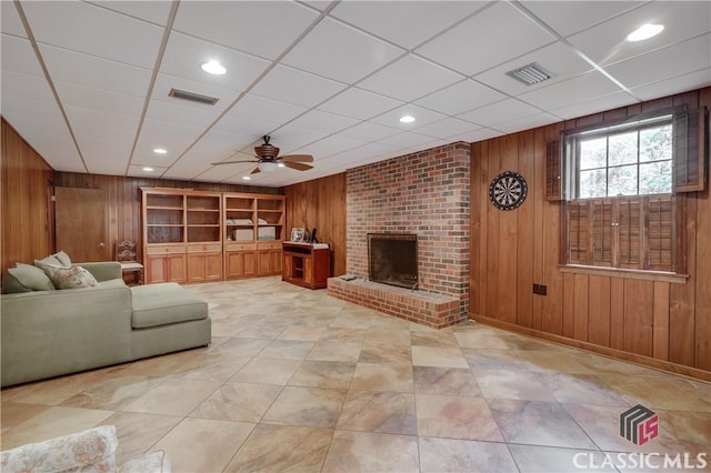 unfurnished living room featuring built in shelves, a fireplace, ceiling fan, and wood walls