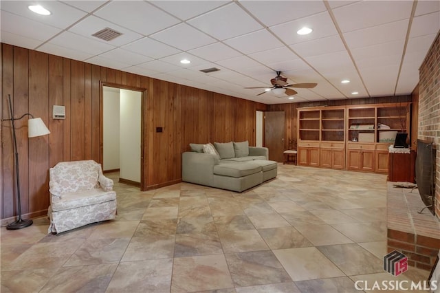 living room with wooden walls, a paneled ceiling, ceiling fan, and built in shelves