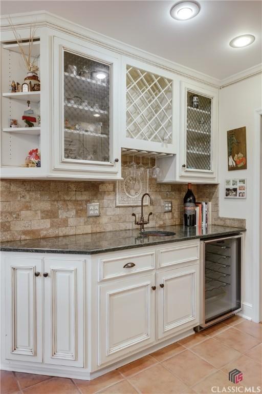 bar featuring sink, tasteful backsplash, light tile patterned floors, beverage cooler, and white cabinets