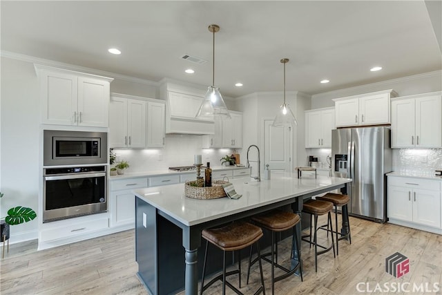 kitchen featuring stainless steel appliances, a kitchen island with sink, hanging light fixtures, and white cabinets