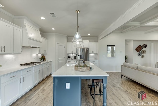 kitchen with appliances with stainless steel finishes, beamed ceiling, white cabinetry, sink, and a kitchen island with sink