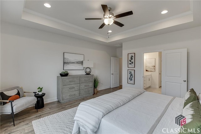 bedroom with connected bathroom, a tray ceiling, light hardwood / wood-style flooring, and ceiling fan