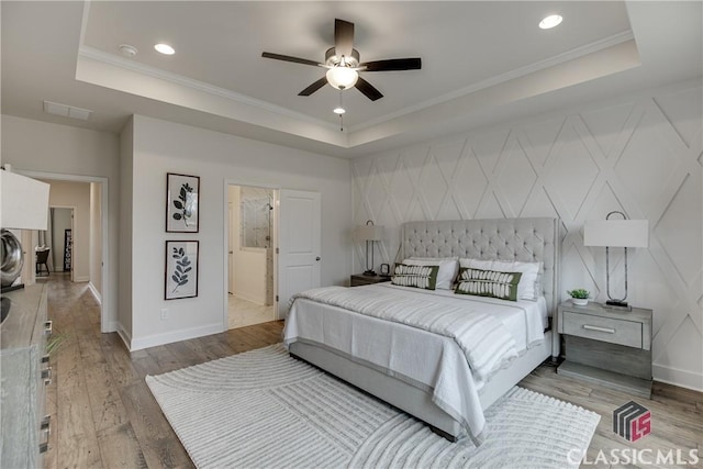 bedroom featuring hardwood / wood-style floors, a raised ceiling, ceiling fan, and ensuite bathroom