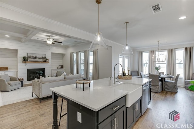 kitchen with sink, coffered ceiling, an island with sink, decorative light fixtures, and beamed ceiling