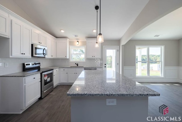 kitchen featuring stainless steel appliances, a kitchen island, pendant lighting, and white cabinets