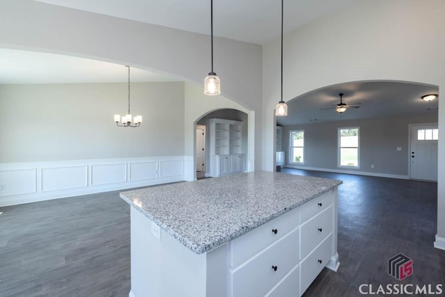 kitchen featuring ceiling fan with notable chandelier, decorative light fixtures, white cabinetry, a center island, and light stone countertops