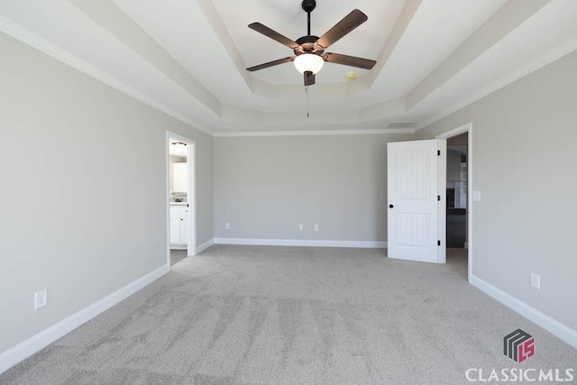 empty room featuring a raised ceiling, ornamental molding, light colored carpet, and ceiling fan