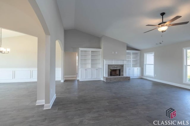 unfurnished living room with vaulted ceiling, dark hardwood / wood-style floors, built in features, a fireplace, and ceiling fan with notable chandelier