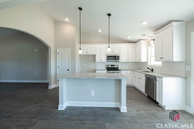 kitchen featuring lofted ceiling, stainless steel appliances, a center island, light stone countertops, and white cabinets