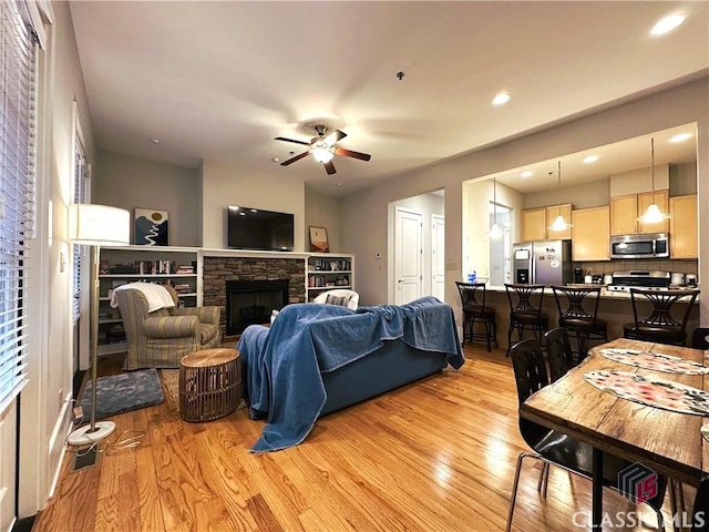 living room featuring ceiling fan, a fireplace, and light hardwood / wood-style flooring