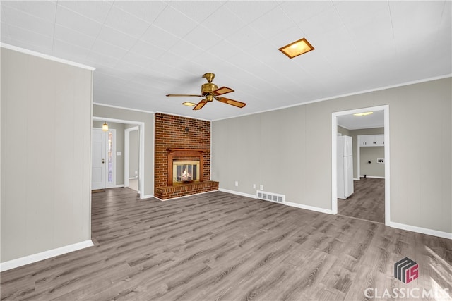 unfurnished living room featuring a brick fireplace, crown molding, ceiling fan, and light wood-type flooring