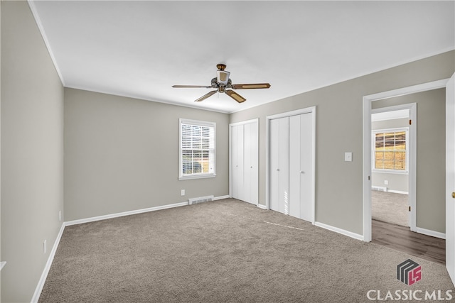 unfurnished bedroom featuring ceiling fan, carpet, and two closets