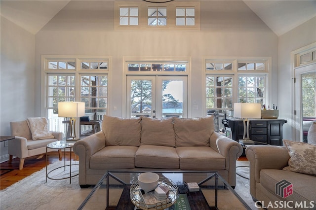 living room with wood-type flooring, high vaulted ceiling, and french doors