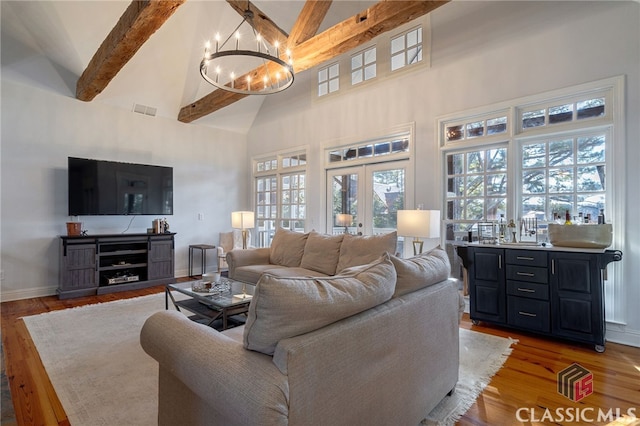 living room featuring high vaulted ceiling, beamed ceiling, french doors, a notable chandelier, and light hardwood / wood-style flooring