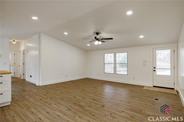 unfurnished living room with lofted ceiling, a wealth of natural light, light hardwood / wood-style floors, and ceiling fan