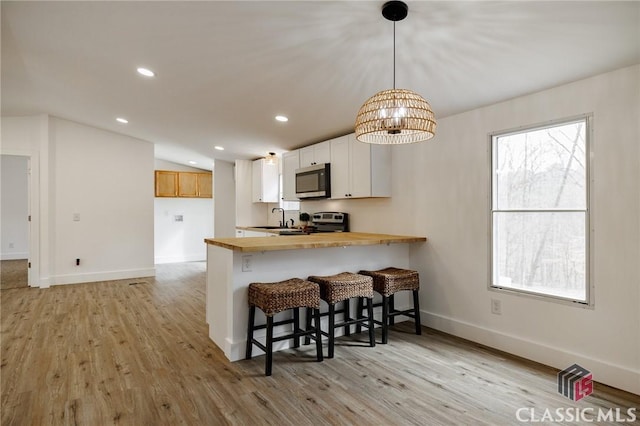 kitchen with a breakfast bar, white cabinetry, stainless steel appliances, decorative light fixtures, and kitchen peninsula