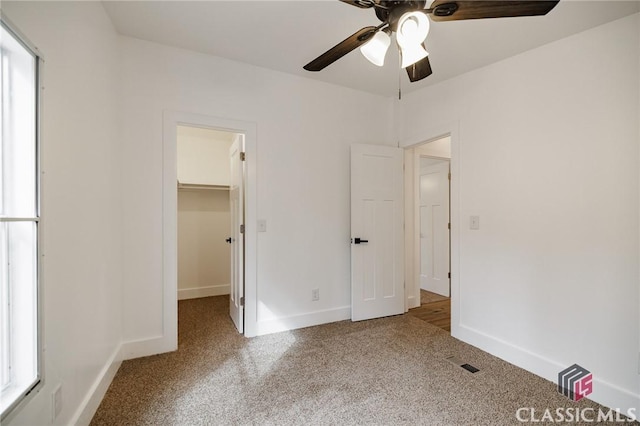 unfurnished bedroom featuring a walk in closet, carpet floors, ceiling fan, and a closet