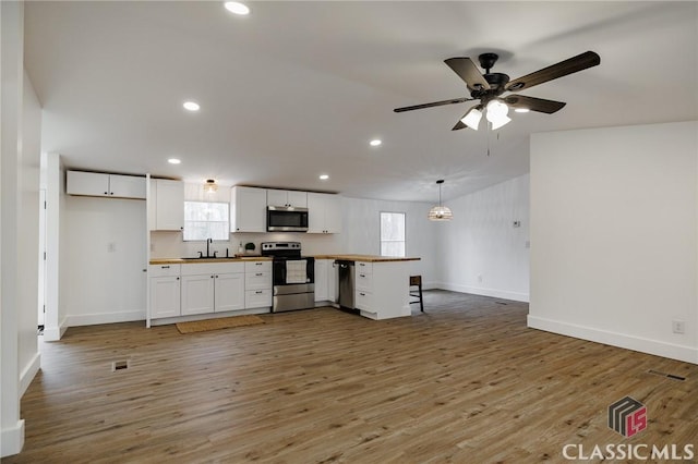 kitchen with sink, white cabinetry, stainless steel appliances, wood-type flooring, and decorative light fixtures