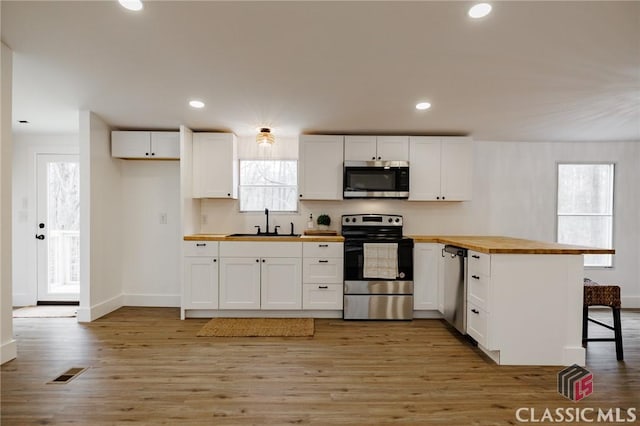 kitchen with sink, appliances with stainless steel finishes, white cabinetry, a kitchen bar, and wood counters