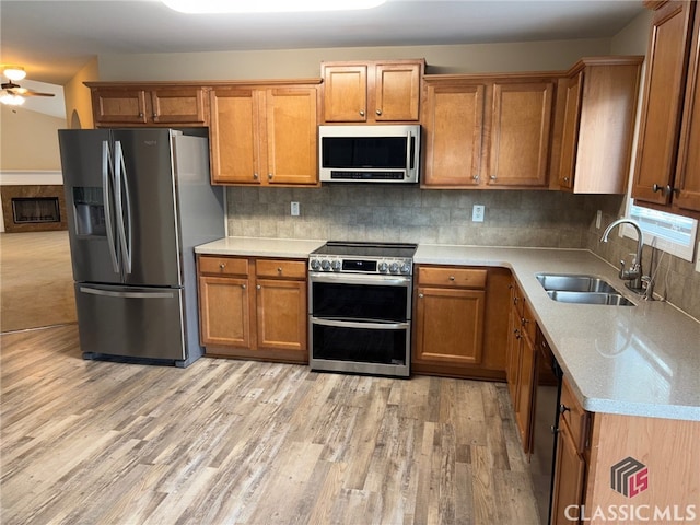 kitchen featuring appliances with stainless steel finishes, tasteful backsplash, sink, ceiling fan, and light hardwood / wood-style flooring