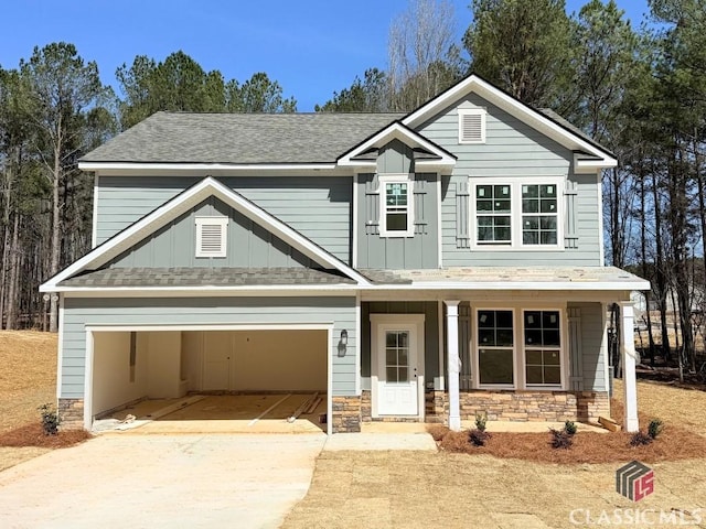 view of front of home with board and batten siding, concrete driveway, roof with shingles, a garage, and stone siding