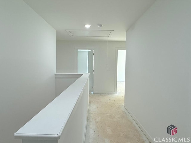 hall with an upstairs landing, concrete flooring, and attic access